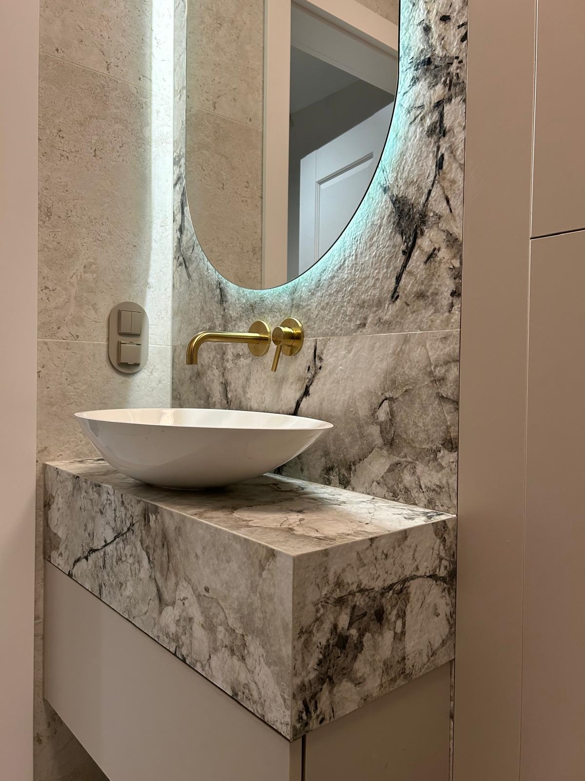 Elegancka łazienka z umywalką nablatową, marmurowym blatem i podświetlanym lustrem. Złota armatura dodaje luksusowego charakteru.
