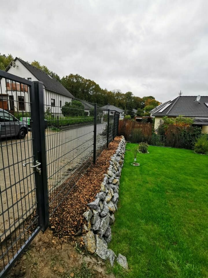 Otwarta brama wjazdowa z metalowych paneli w Gubinie, widok na posesję z trawnikiem i kamiennym murkiem wzdłuż ogrodzenia.