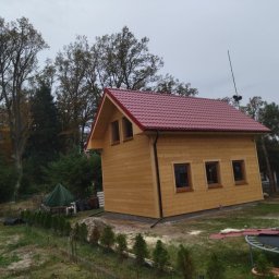 Piotr łozowski alt- drew - Nowo wybudowany drewniany domek letniskowy z czerwonym dachem na działce z drzewami, widok z boku, z widocznymi elementami wykończeniowymi.