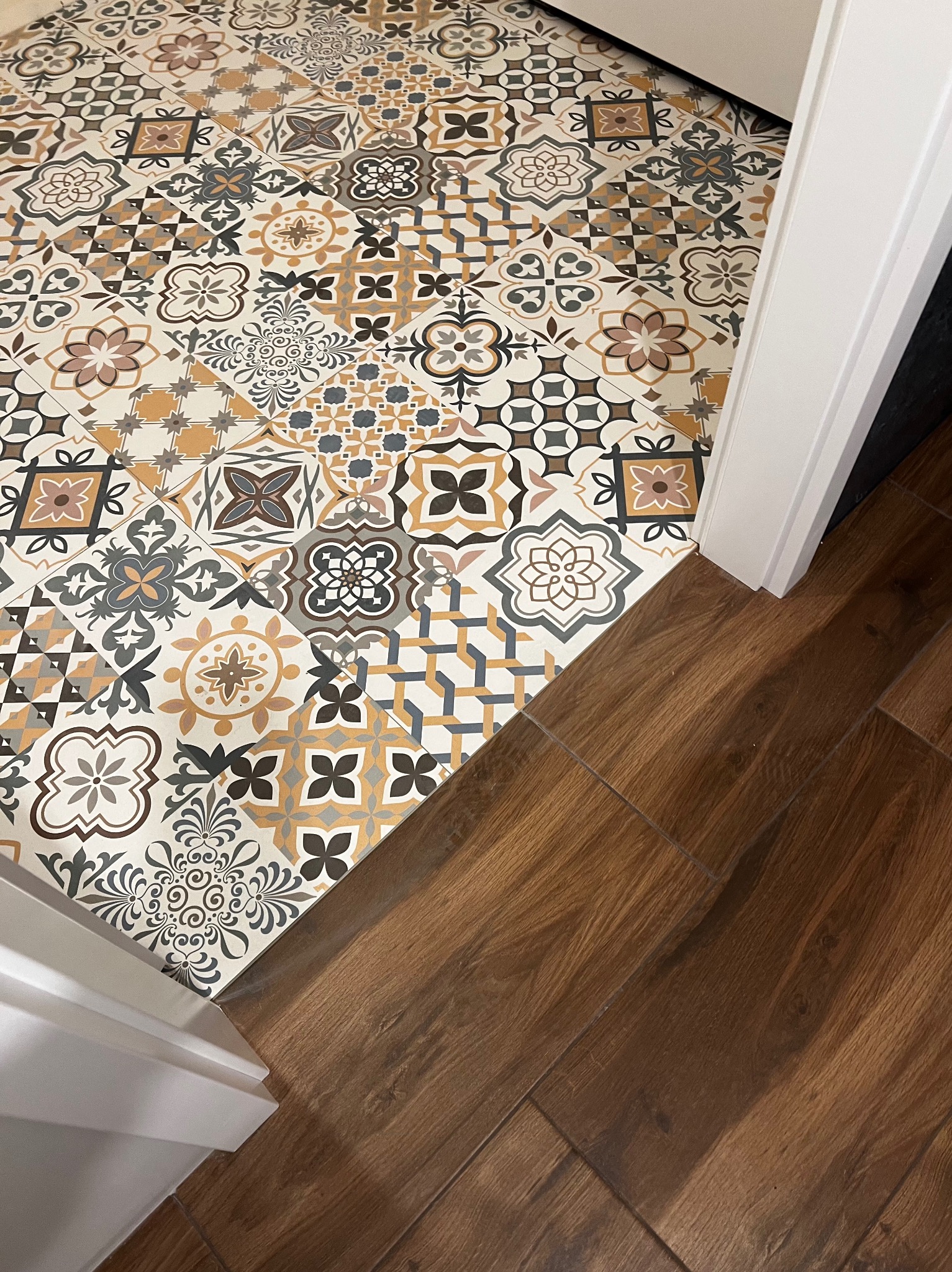 Połączenie podłogi z płytek patchworkowych w odcieniach beżu, brązu i szarości z panelami imitującymi drewno przy białej futrynie drzwi.