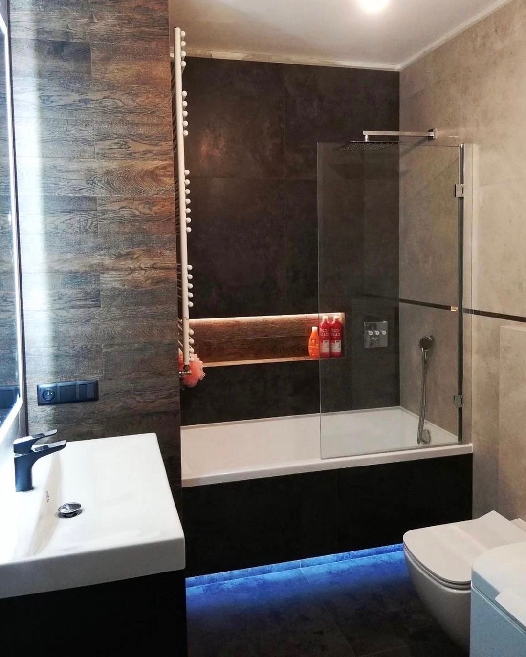 Nowoczesna łazienka z ciemnymi płytkami imitującymi drewno, podświetlaną wanną i minimalistyczną umywalką z czarną baterią.