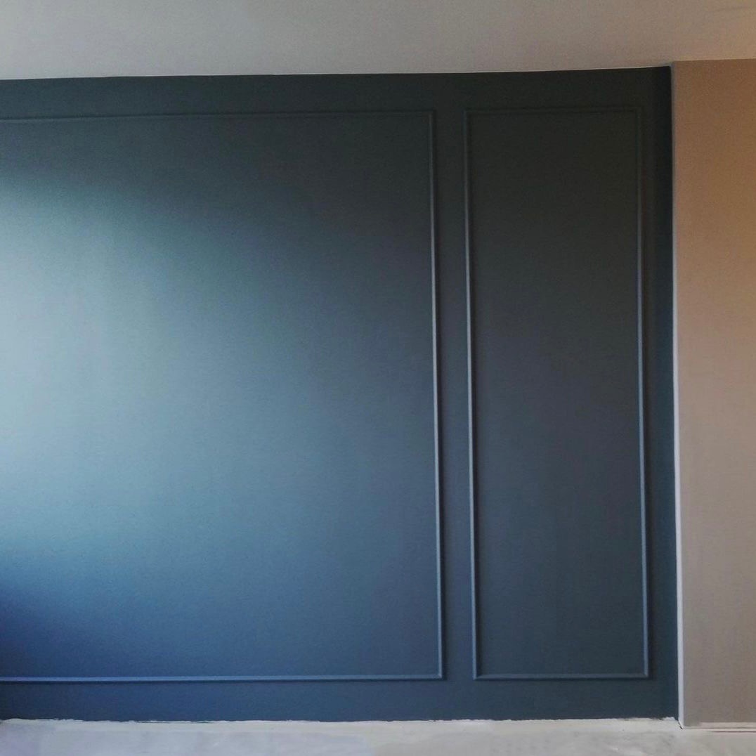 Ściana pomalowana na ciemny odcień niebieskiego z dekoracyjnymi listwami tworzącymi prostokątne panele, widoczny fragment sąsiedniej ściany w kolorze beżowym.