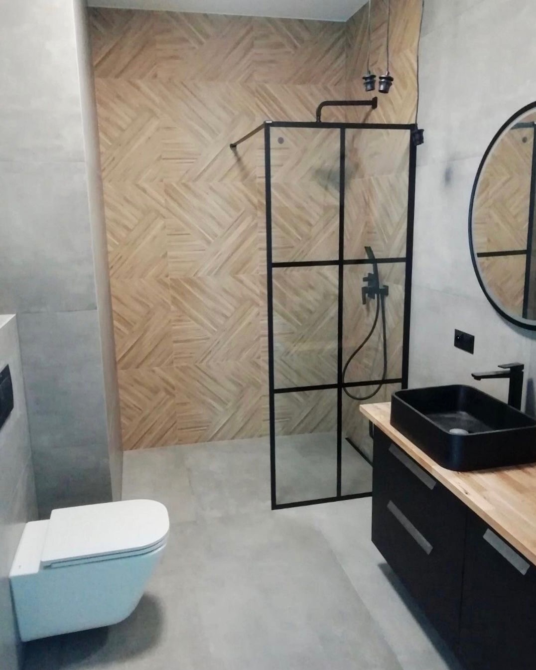 Nowoczesna łazienka w Warszawie z kabiną prysznicową typu walk-in z czarnymi ramami, umywalką nablatową w kolorze czarnym, drewnianym blatem i mozaiką drewnopodobną na ścianie pod prysznicem.