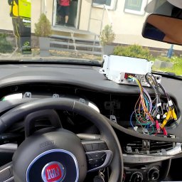 JanSerwis.pl - Demontaż deski rozdzielczej samochodu Fiat w celu podłączenia nowego radia samochodowego z widocznymi kablami i złączami RCA.