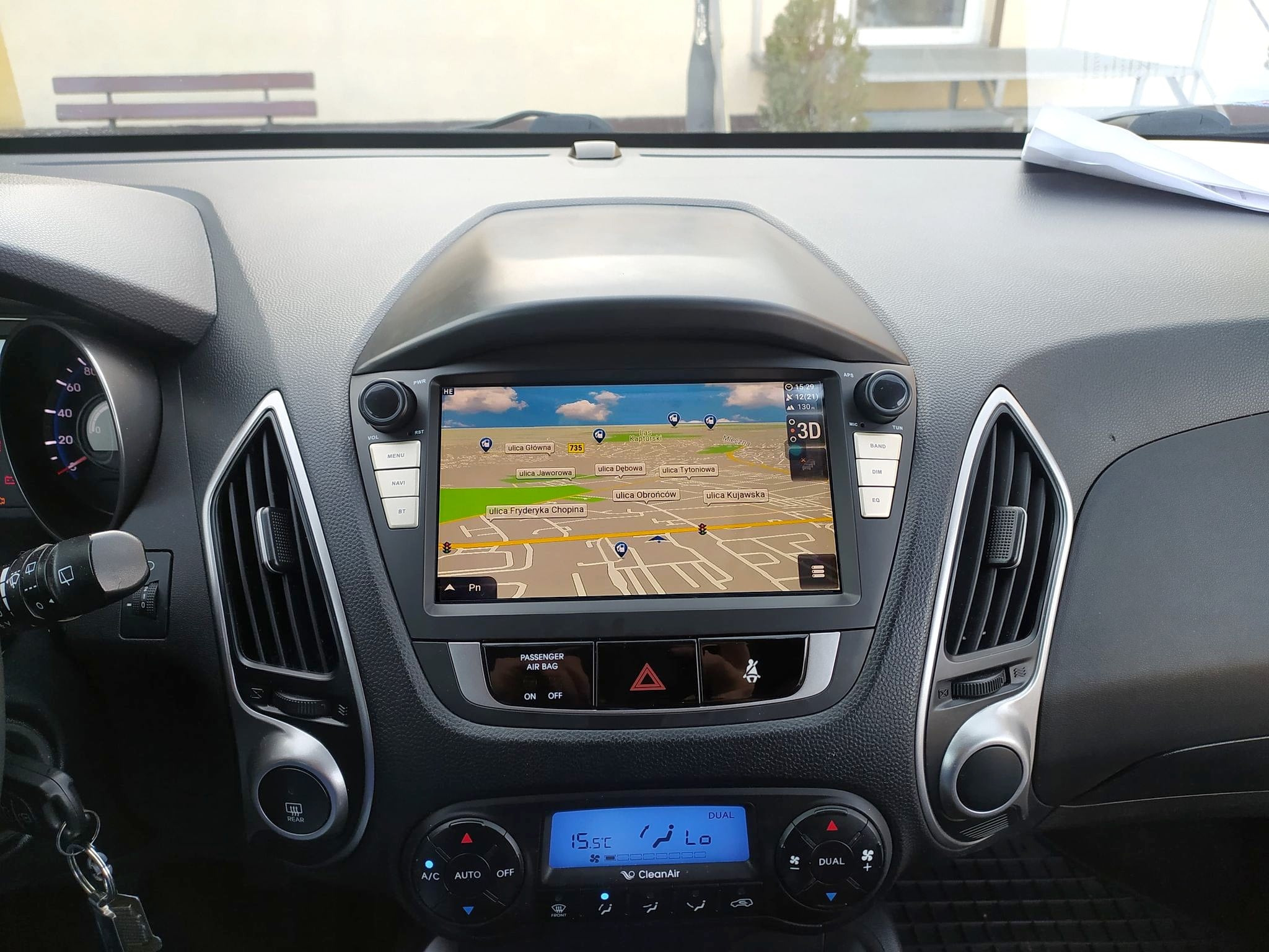 Wnętrze samochodu z włączoną nawigacją GPS, wyświetlającą mapę ulic. Widoczny panel klimatyzacji z temperaturą 15.5 stopni Celsjusza, przyciski sterowania i kluczyki w stacyjce.