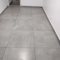 Szare, matowe płytki podłogowe ułożone w nowym pomieszczeniu z białymi ścianami i widocznym wejściem do innego pomieszczenia w tle.