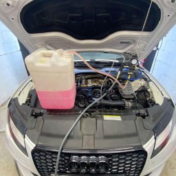 Mechanika Pojazdowa Grzegorz Pater - Białe Audi z otwartą maską podczas wymiany płynu chłodniczego; widoczny pojemnik z różowym płynem i podłączone przewody.