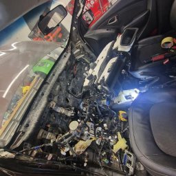 Mechanika Pojazdowa Grzegorz Pater - Wnętrze samochodu z widoczną zdemontowaną deską rozdzielczą, liczne kable i elementy elektroniczne w trakcie naprawy lub diagnostyki.