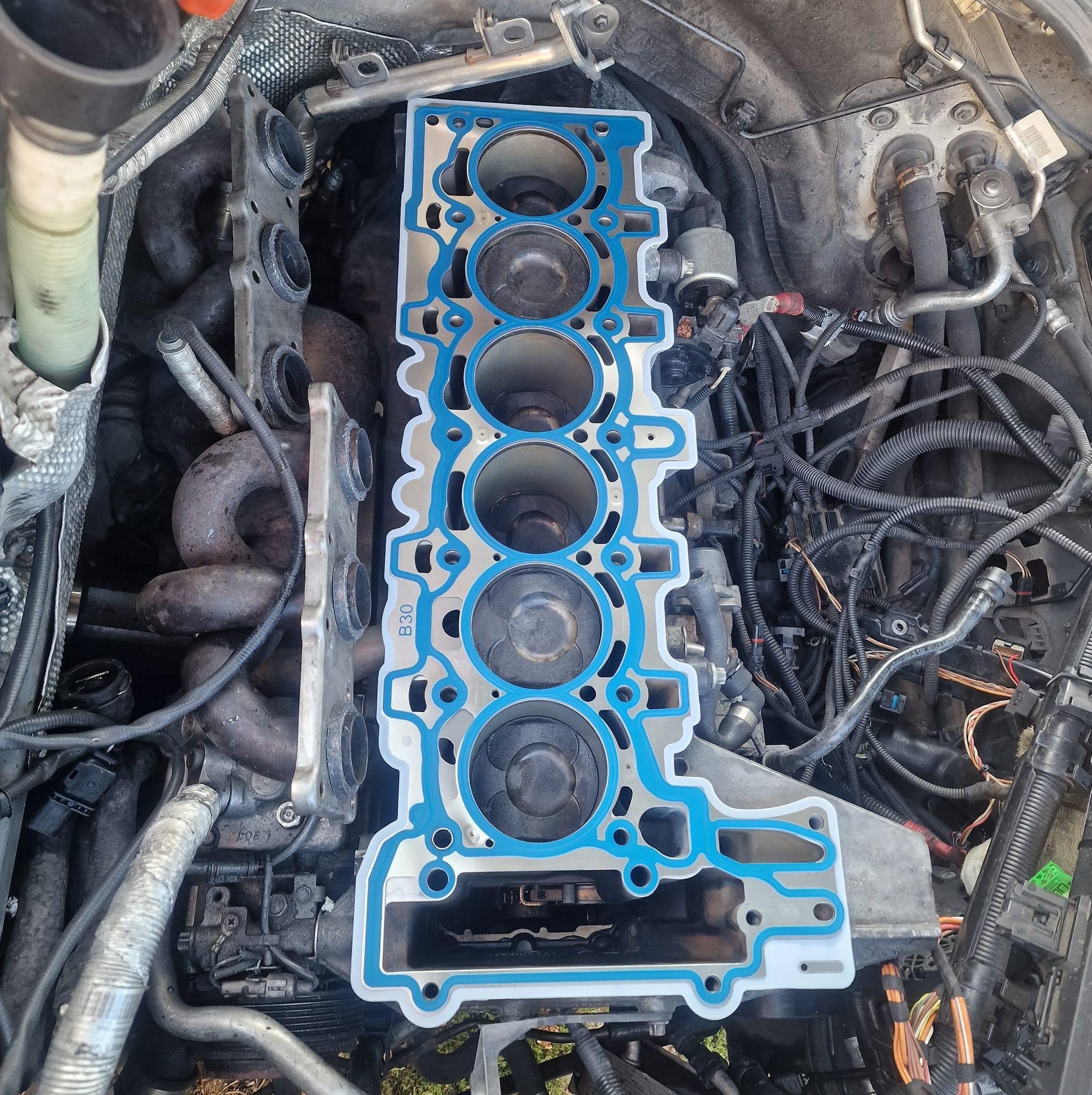 Zdjęcie silnika samochodowego w trakcie naprawy w Nowym Korczynie, widoczny blok silnika z założoną uszczelką głowicy w kolorze niebieskim i srebrnym. W tle wiązki przewodów i inne elementy osprzętu.