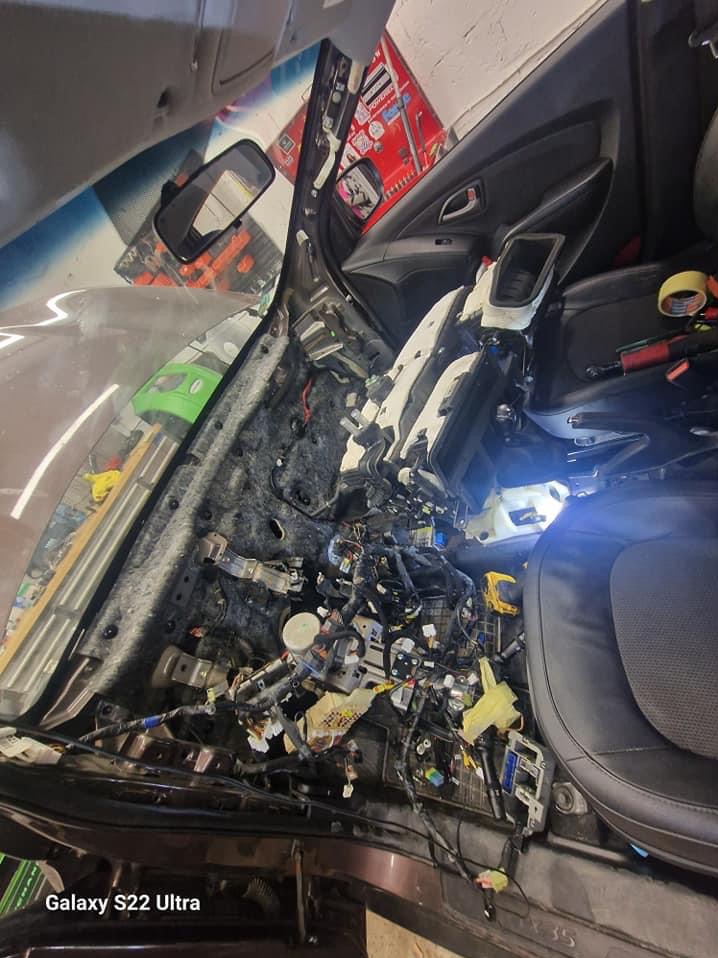 Wnętrze samochodu z widoczną zdemontowaną deską rozdzielczą, liczne kable i elementy elektroniczne w trakcie naprawy lub diagnostyki.