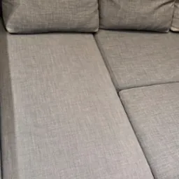 Szary narożnik z tkaniny o widocznej strukturze, jasne drewniane panele podłogowe w dolnym rogu kadru.