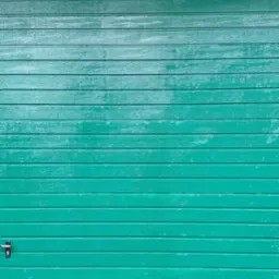 Turkusowa, pozioma brama garażowa z drobnymi zabrudzeniami i czarnym uchwytem po lewej stronie.