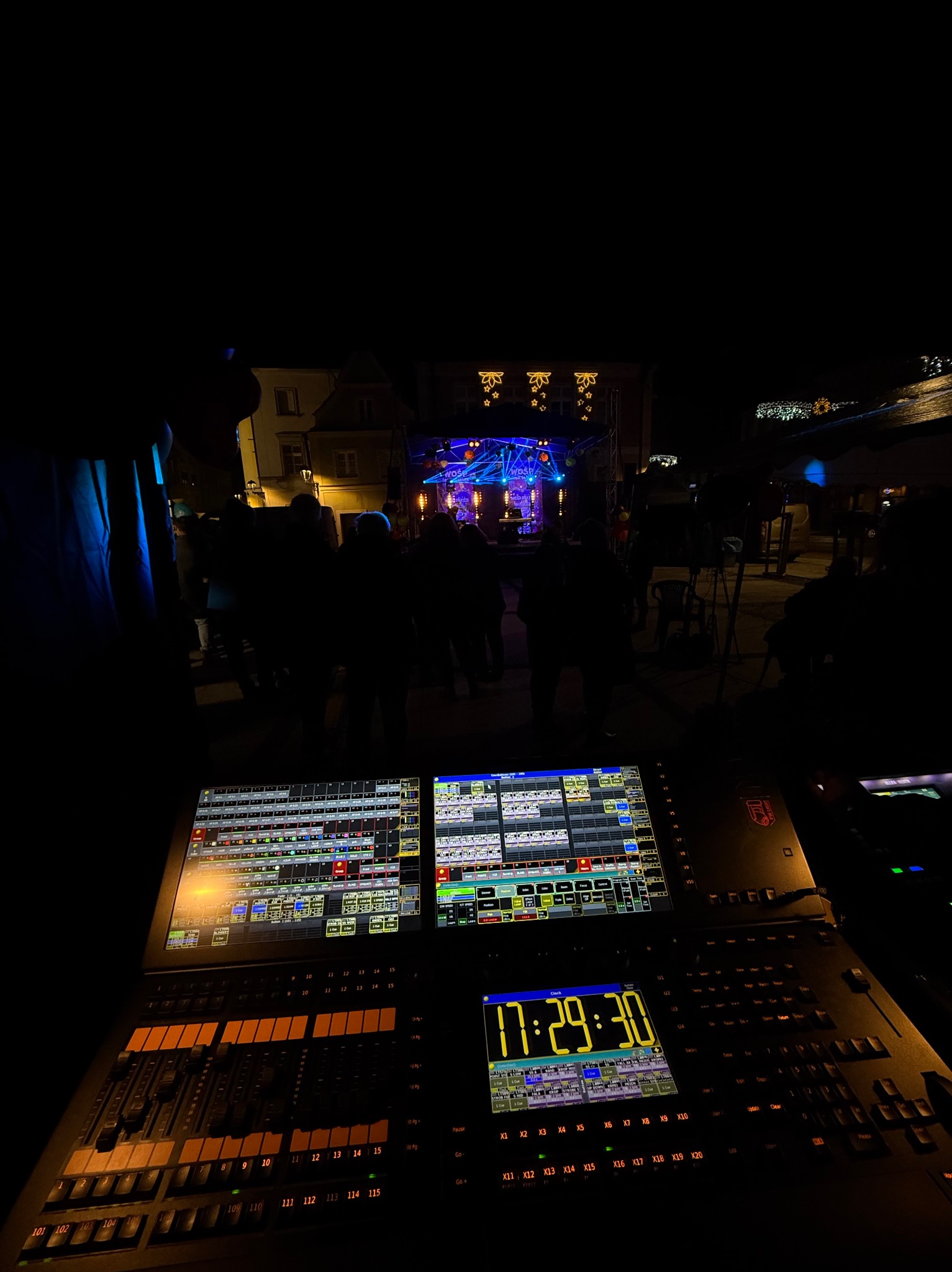 Panel sterowania oświetleniem i dźwiękiem z widokiem na oświetloną scenę podczas wieczornego wydarzenia plenerowego.