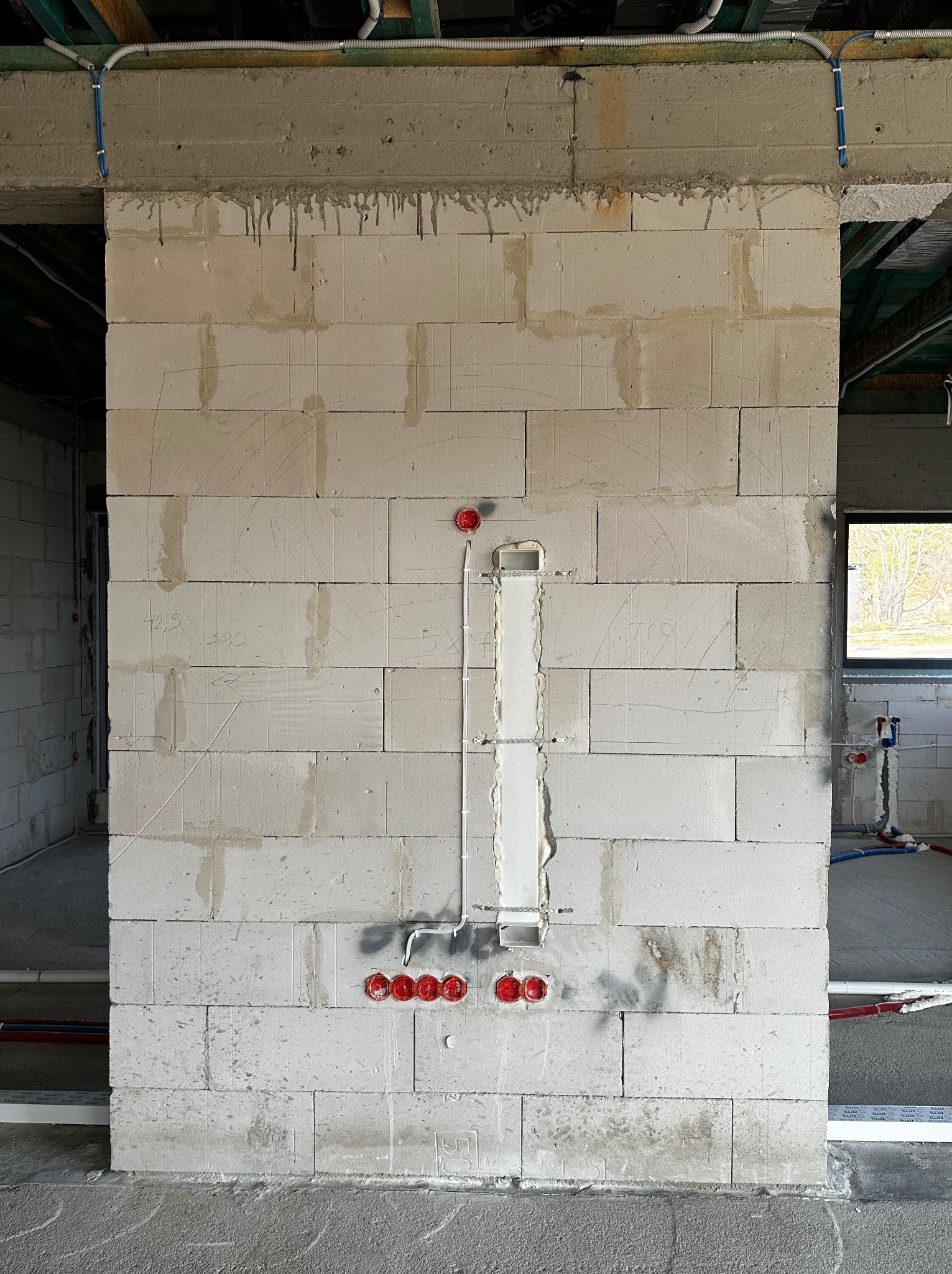 Ściana z betonu komórkowego z wyżłobieniami i puszkami instalacyjnymi pod gniazdka elektryczne. Widoczne przewody i rurki instalacyjne. Surowy stan wykończenia.