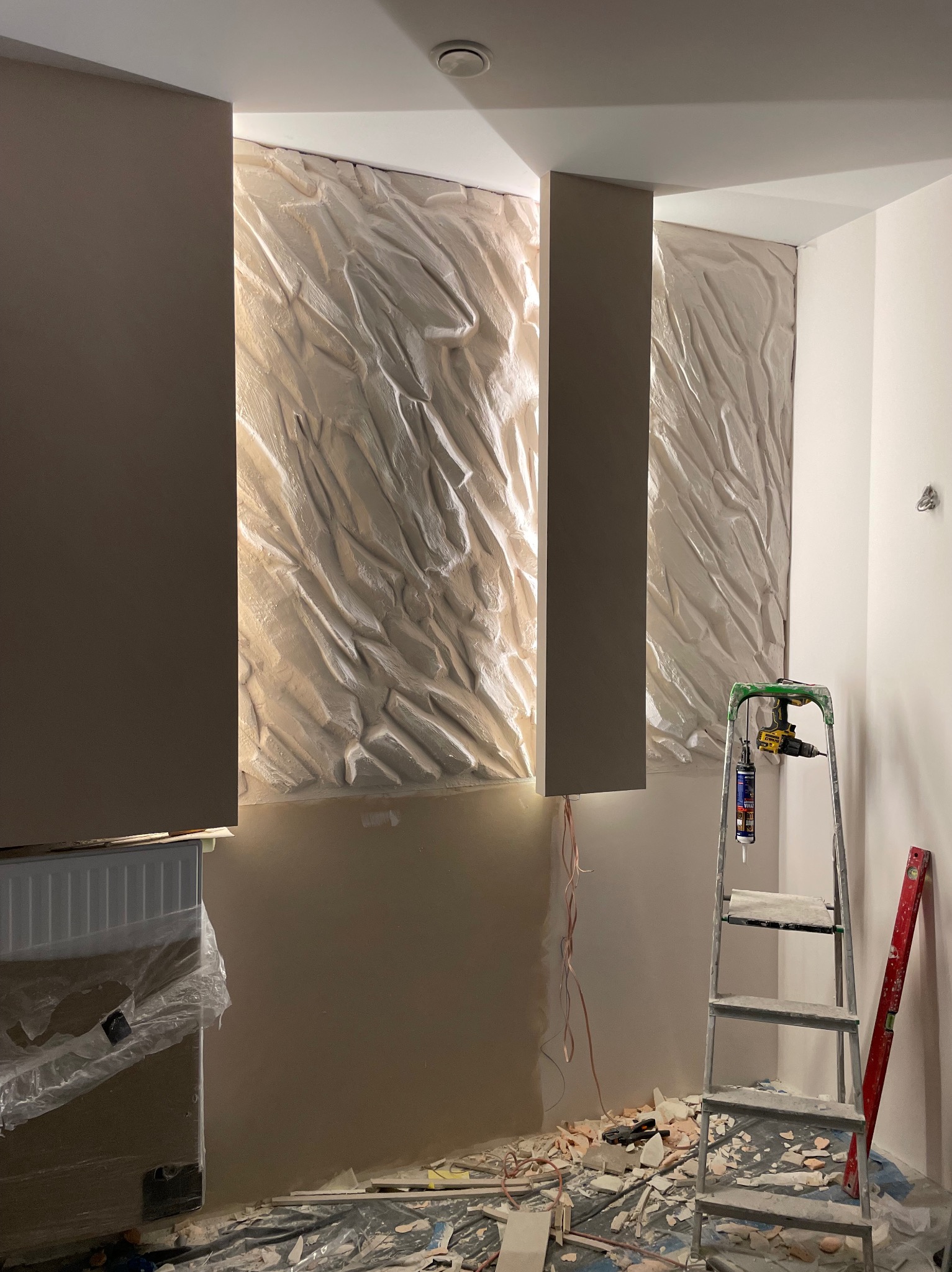 Montaż dekoracyjnych paneli ściennych z podświetleniem LED w trakcie remontu, widoczna drabina, narzędzia i gruz na podłodze.