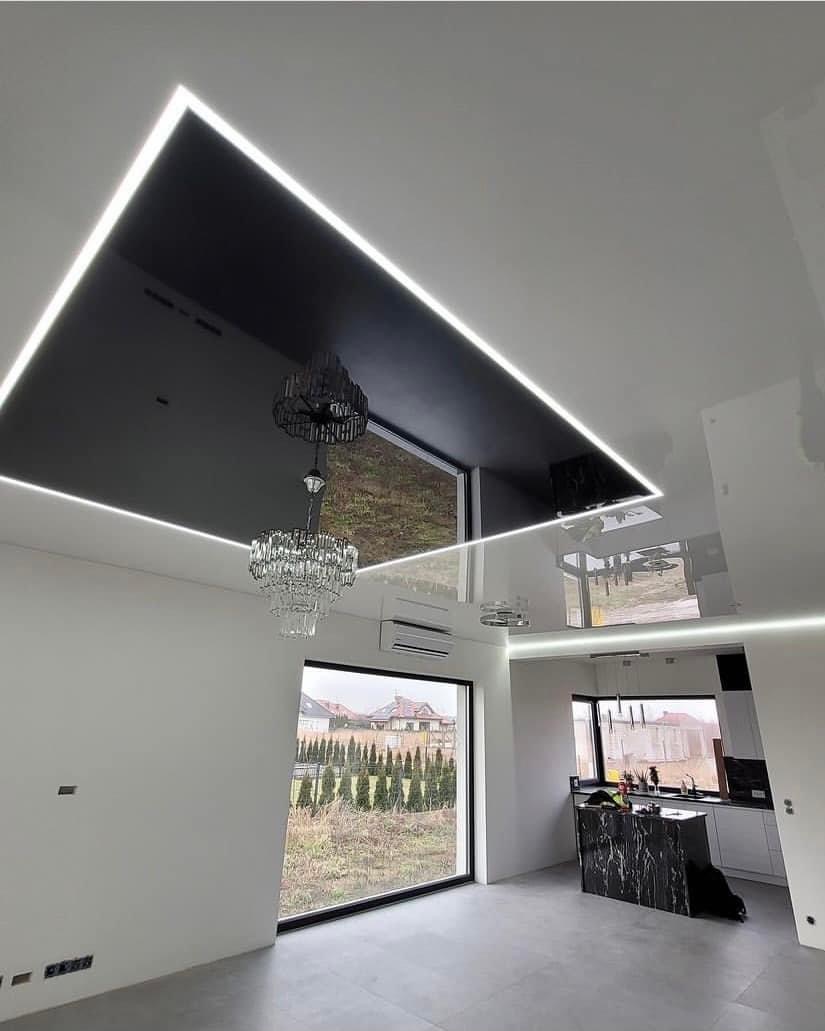 Salon z czarnym podwieszanym sufitem z oświetleniem LED, kryształowym żyrandolem i dużym oknem z widokiem na ogród.