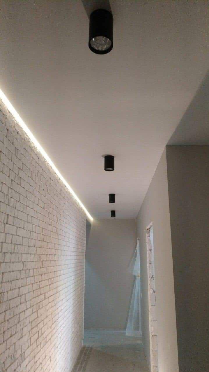 Korytarz z oświetleniem LED wzdłuż ściany z cegły i trzema czarnymi reflektorami sufitowymi.