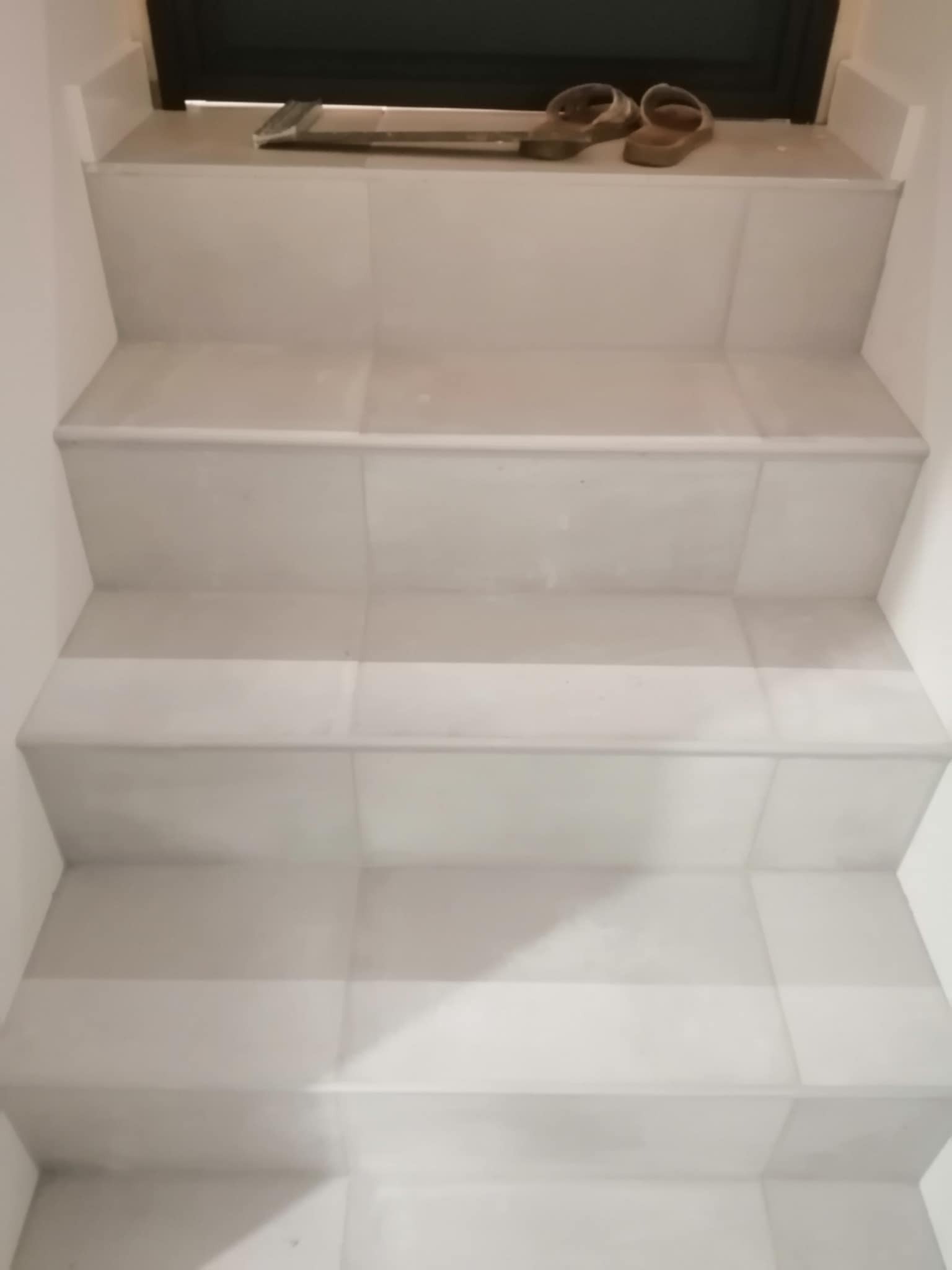 Wykończone, jasne schody wewnątrz budynku, pokryte płytkami ceramicznymi. Na górnym stopniu leżą klapki i narzędzie glazurnicze.