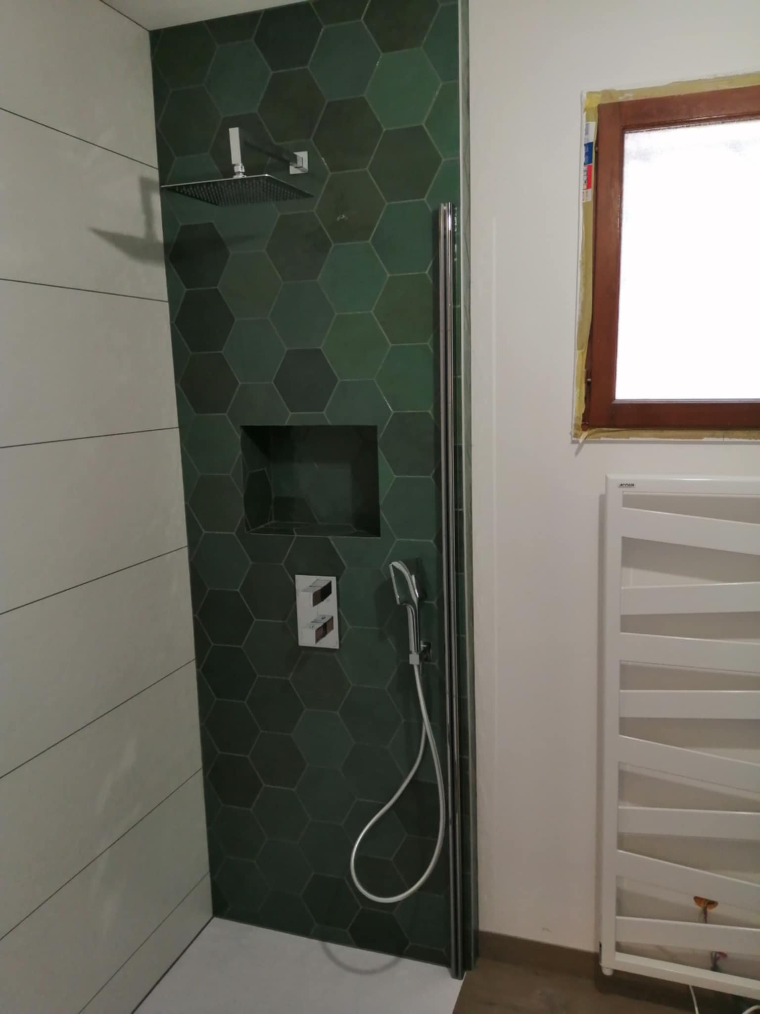 Wykończona kabina prysznicowa z zielonymi, heksagonalnymi płytkami i wnęką w Rzeszowie. Nowoczesny design z białą grzejnik drabinką.