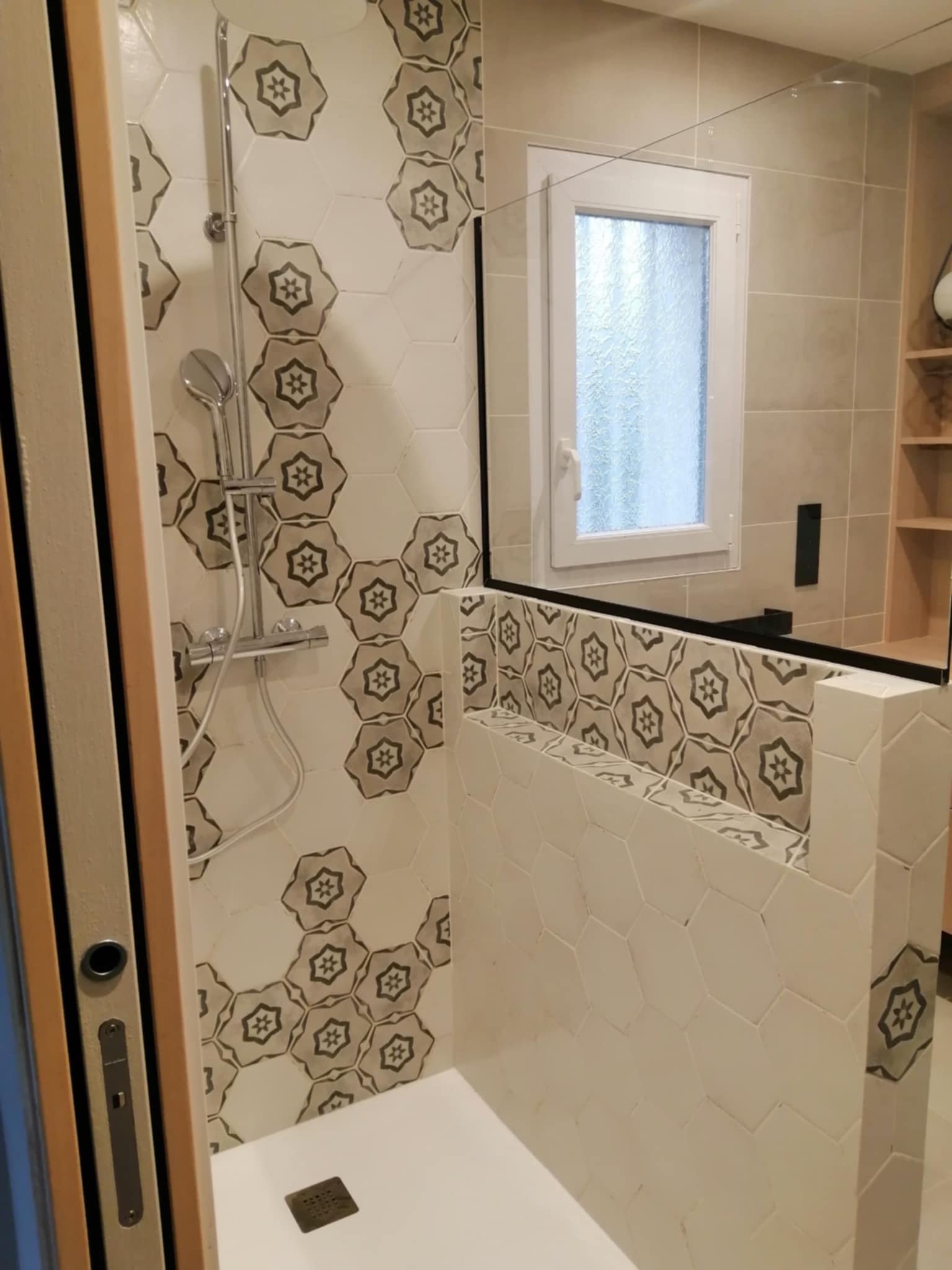 Nowoczesna kabina prysznicowa z heksagonalnymi płytkami w odcieniach bieli i szarości z motywem kwiatowym, szklana szyba i minimalistyczna armatura.