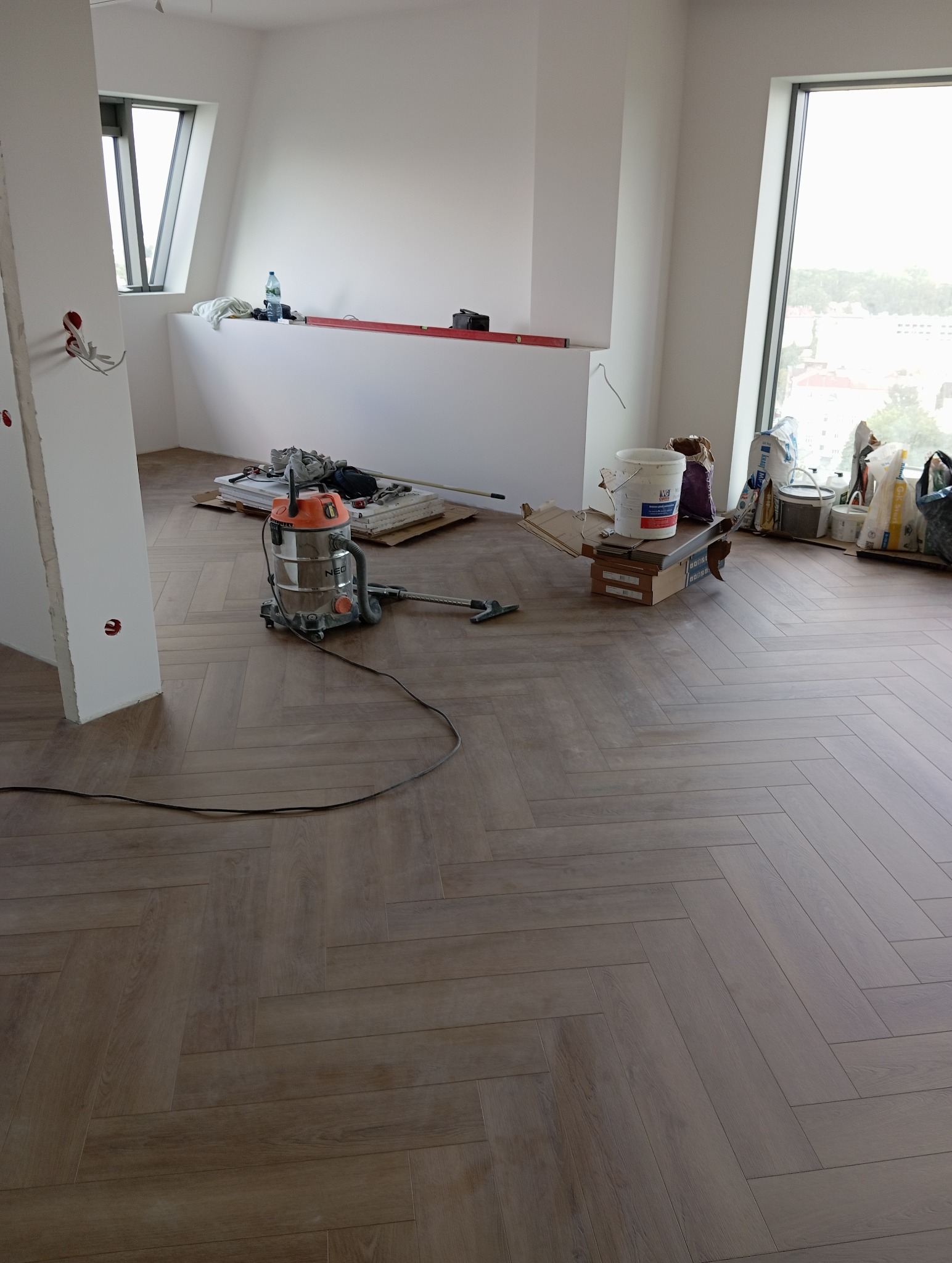Ukończona podłoga z paneli ułożonych w jodełkę, widoczny odkurzacz przemysłowy i narzędzia, remont mieszkania w trakcie wykańczania.