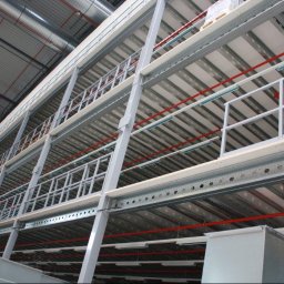 Logis - Wielopoziomowa konstrukcja stalowa w hali magazynowej z metalowymi balustradami i oświetleniem, widok z dołu.