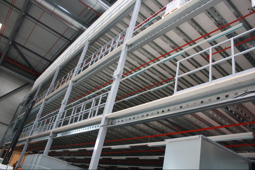 Wielopoziomowa konstrukcja stalowa w hali magazynowej z metalowymi balustradami i oświetleniem, widok z dołu.