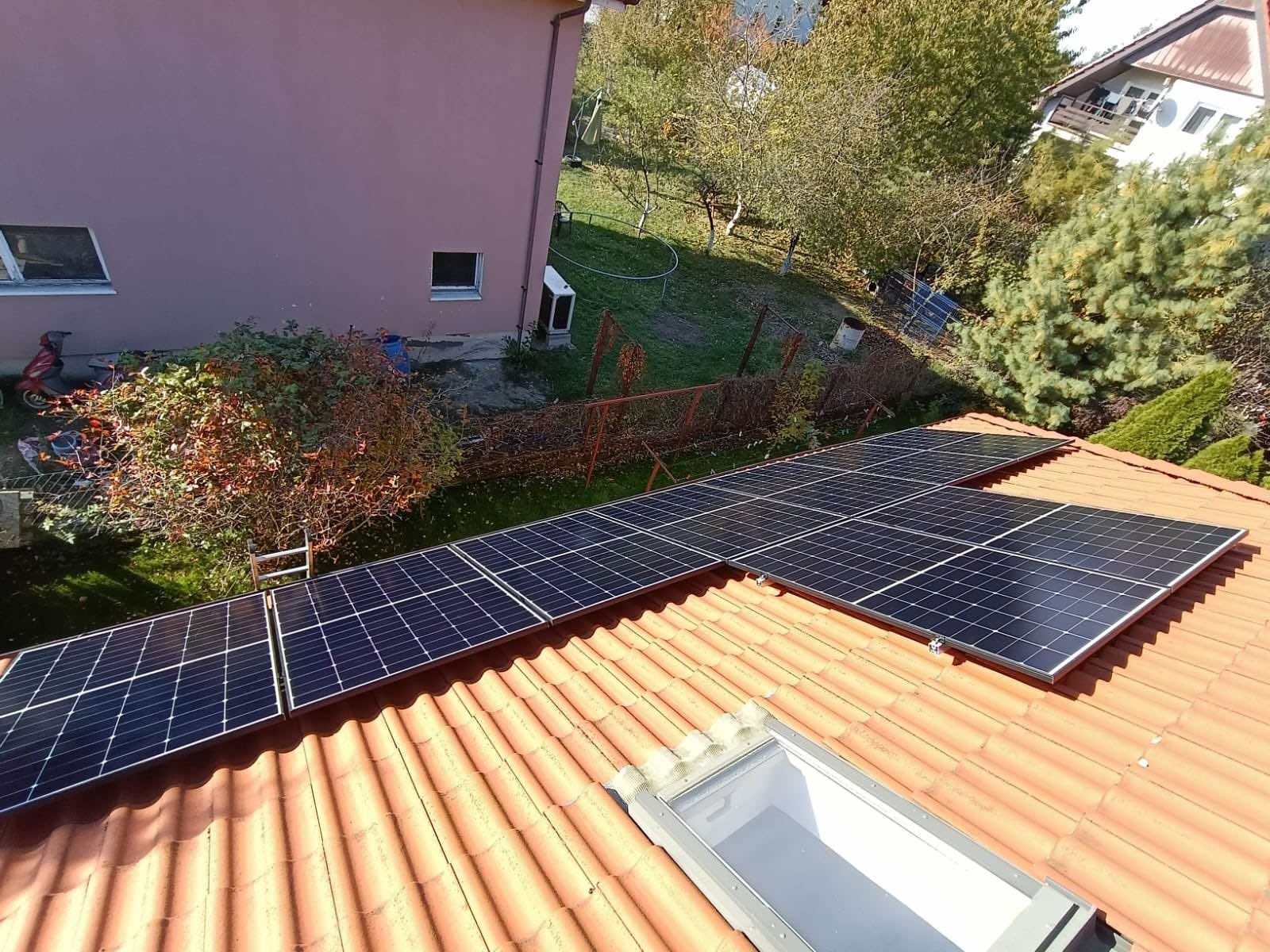 Panele słoneczne zamontowane na dachu z pomarańczowej dachówki, widok z góry na instalację i otoczenie budynku.