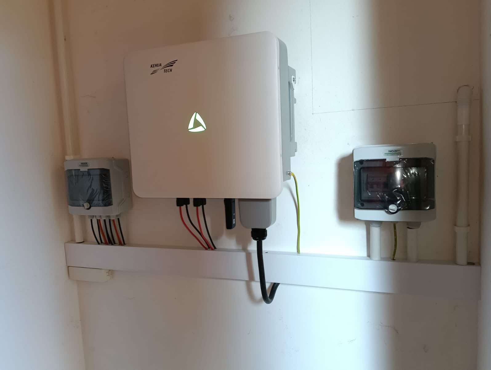 Zamontowany biały inwerter fotowoltaiczny firmy Kehua Tech z podłączonymi kablami i skrzynkami zabezpieczającymi na białej ścianie.