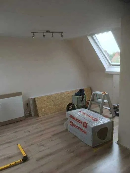 Poddasze w trakcie remontu z oknem dachowym, widoczne płyty OSB, wełna mineralna Rockwool w folii, drabina aluminiowa i narzędzia.