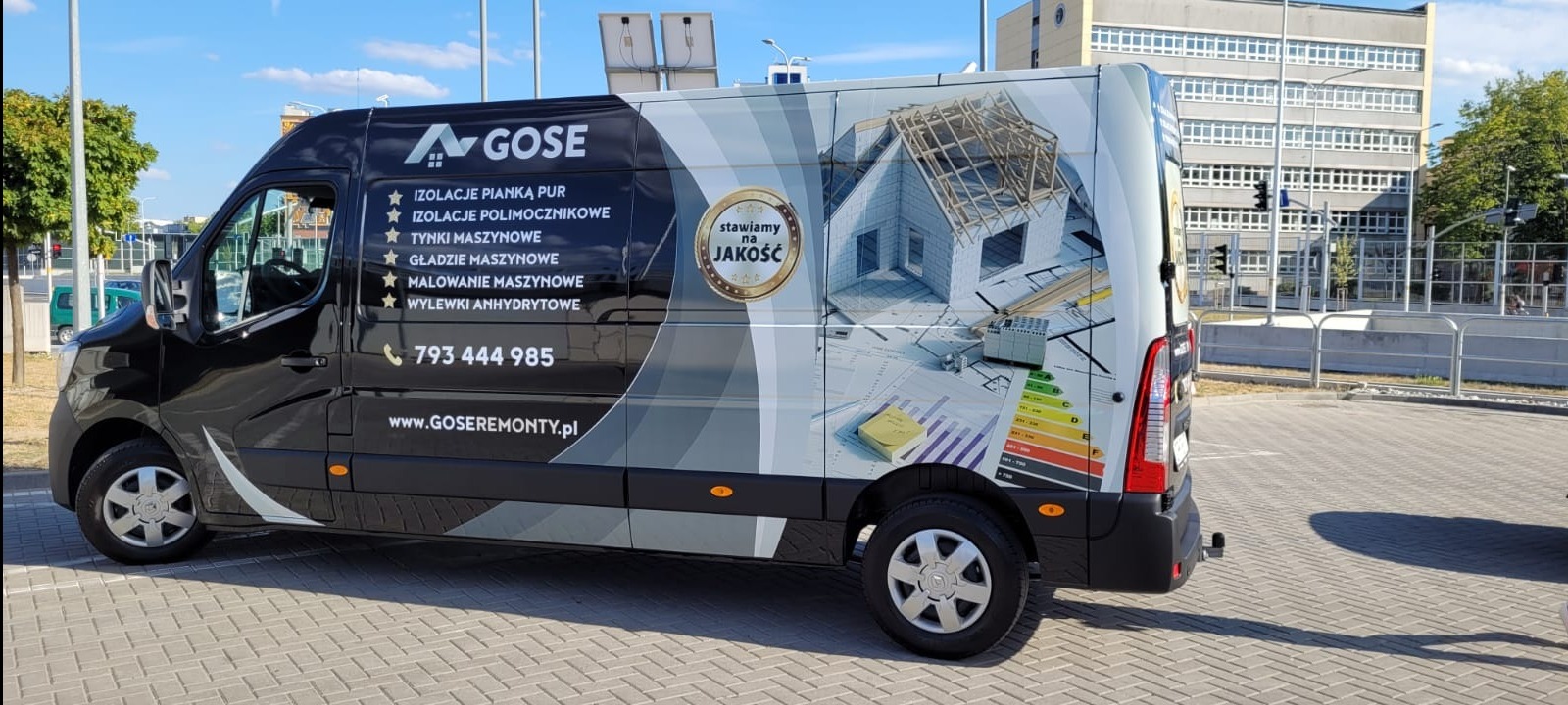Czarny samochód dostawczy firmy GOSE z grafiką przedstawiającą dom w trakcie budowy, materiały budowlane, certyfikat energetyczny i hasłem 'Stawiamy na jakość'.