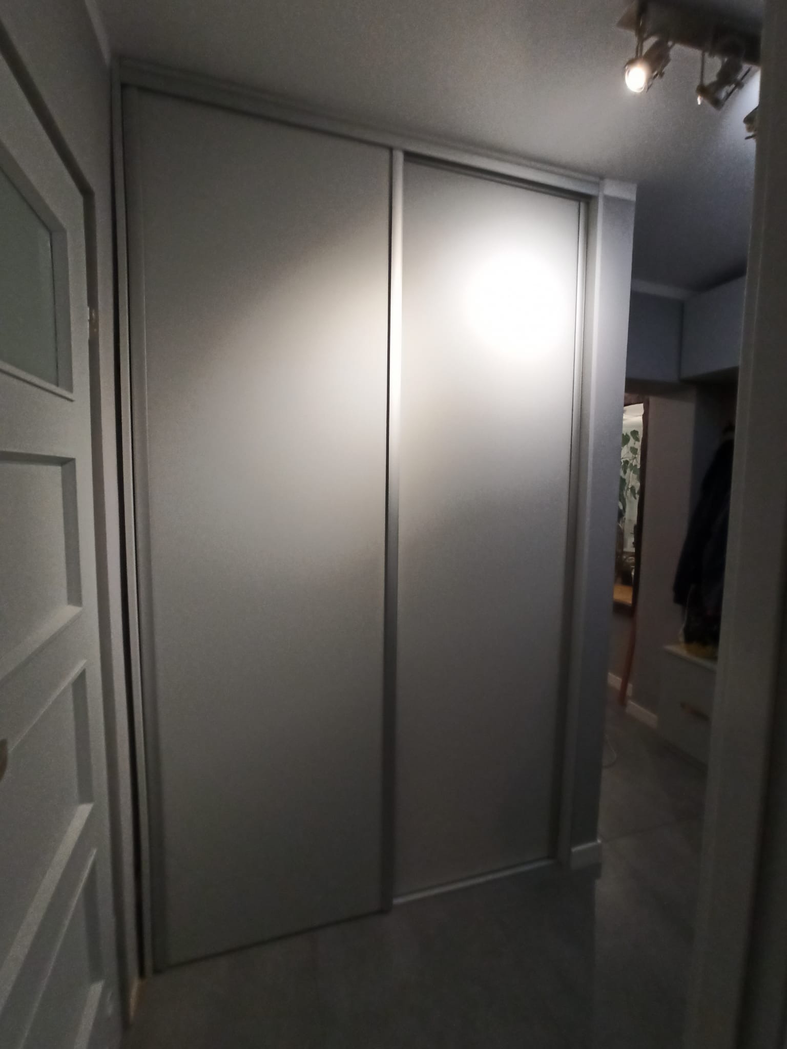 Nowoczesna szafa przesuwna z matowymi, szarymi drzwiami w wąskim korytarzu, widok z bliska na minimalizm i funkcjonalność.