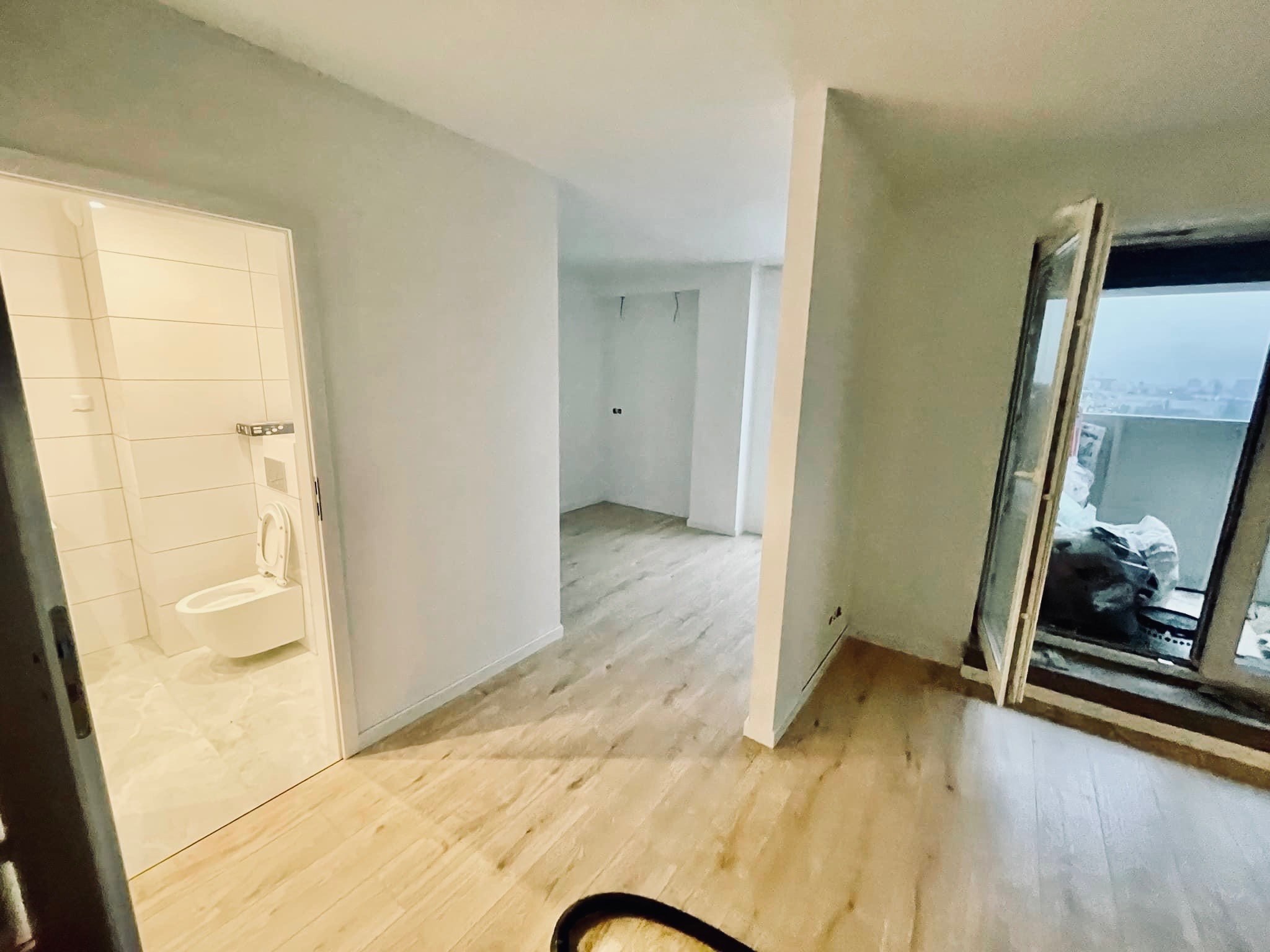 Wnętrze mieszkania w trakcie remontu: widok na nowo wyłożoną podłogę, świeżo pomalowane ściany, wykończoną łazienkę z toaletą oraz balkon z otwartymi drzwiami balkonowymi i workami z materiałami...