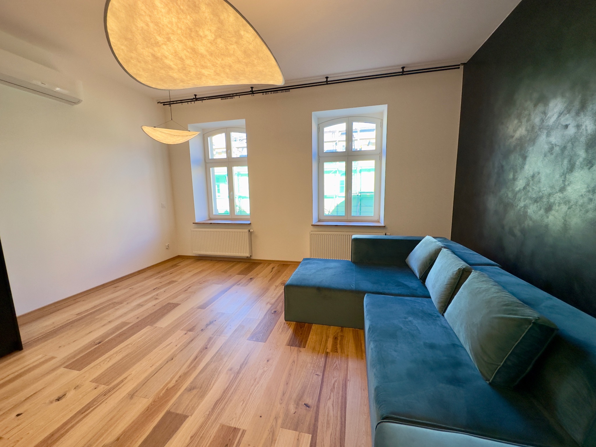 Nowoczesny salon z modułową, turkusową sofą, drewnianą podłogą i designerskim oświetleniem sufitowym.