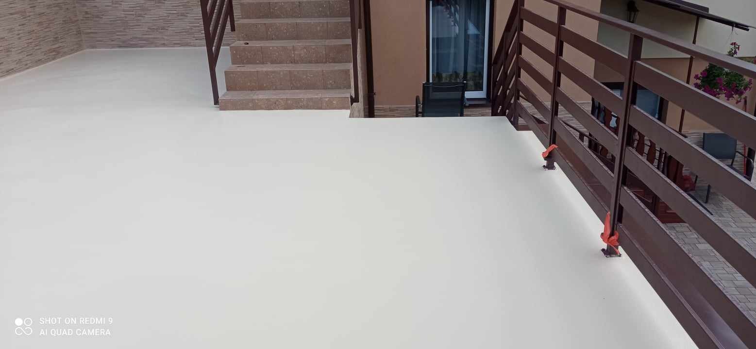 Biała, gładka powierzchnia balkonu z brązową balustradą, widoczne schody z brązowych płytek prowadzące w górę, elementy zabezpieczające balustradę w kolorze pomarańczowym.