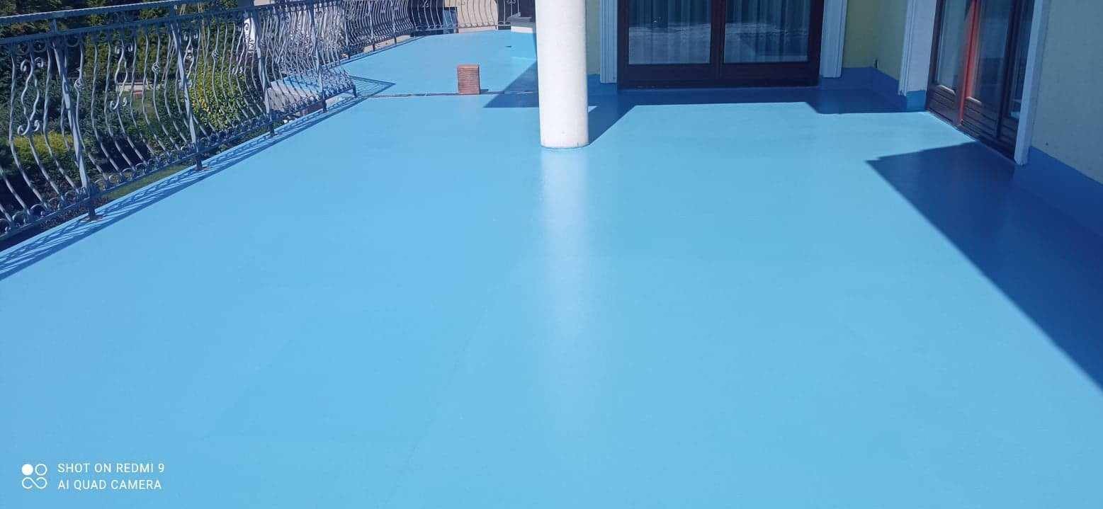 Błękitna, jednolita posadzka żywiczna na balkonie z metalową balustradą i kolumnami, widok z góry.