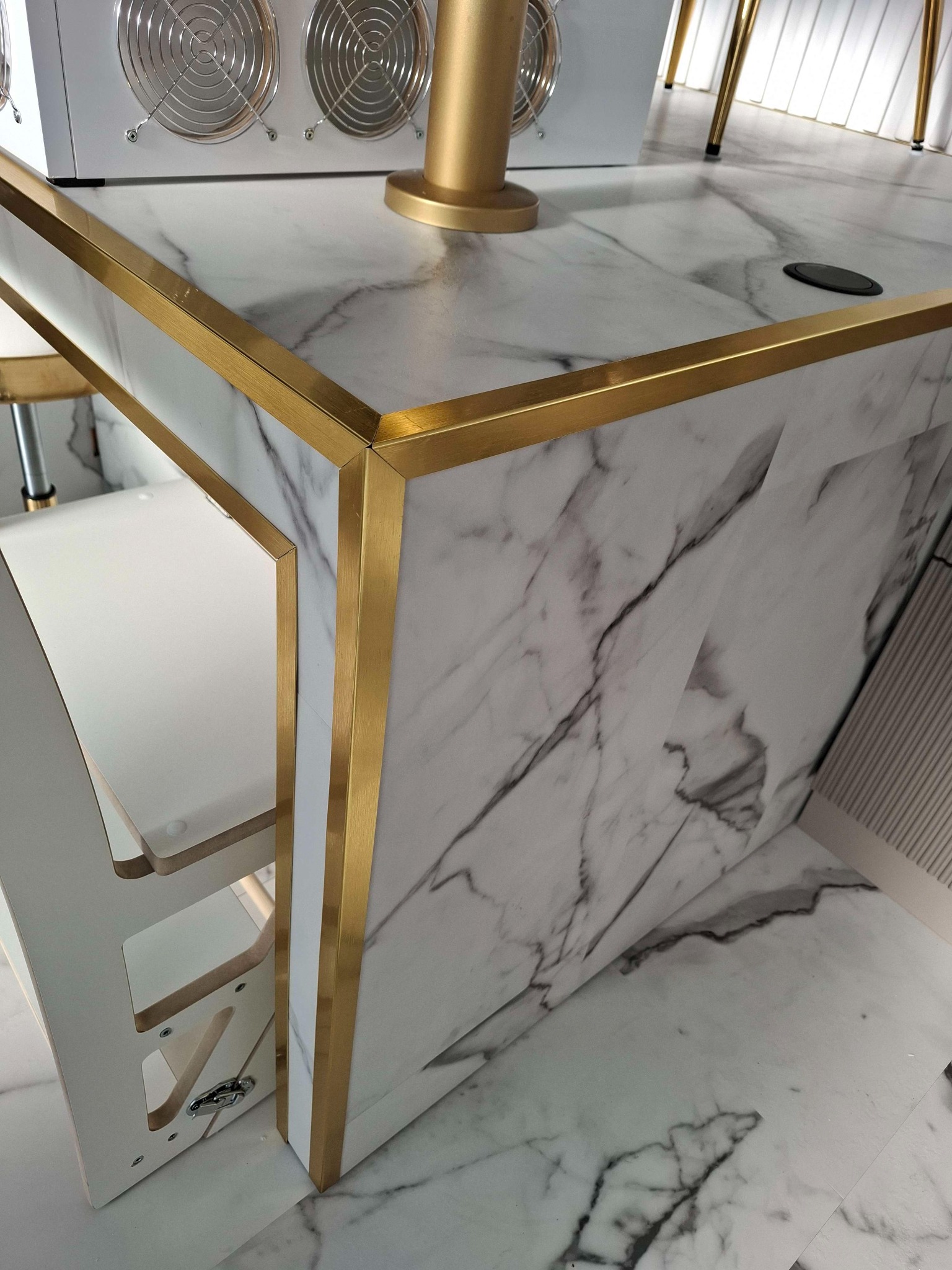 Fragment blatu z marmurowym wzorem i złotymi krawędziami, widoczne białe wentylatory i element metalowej konstrukcji, całość w nowoczesnym stylu.