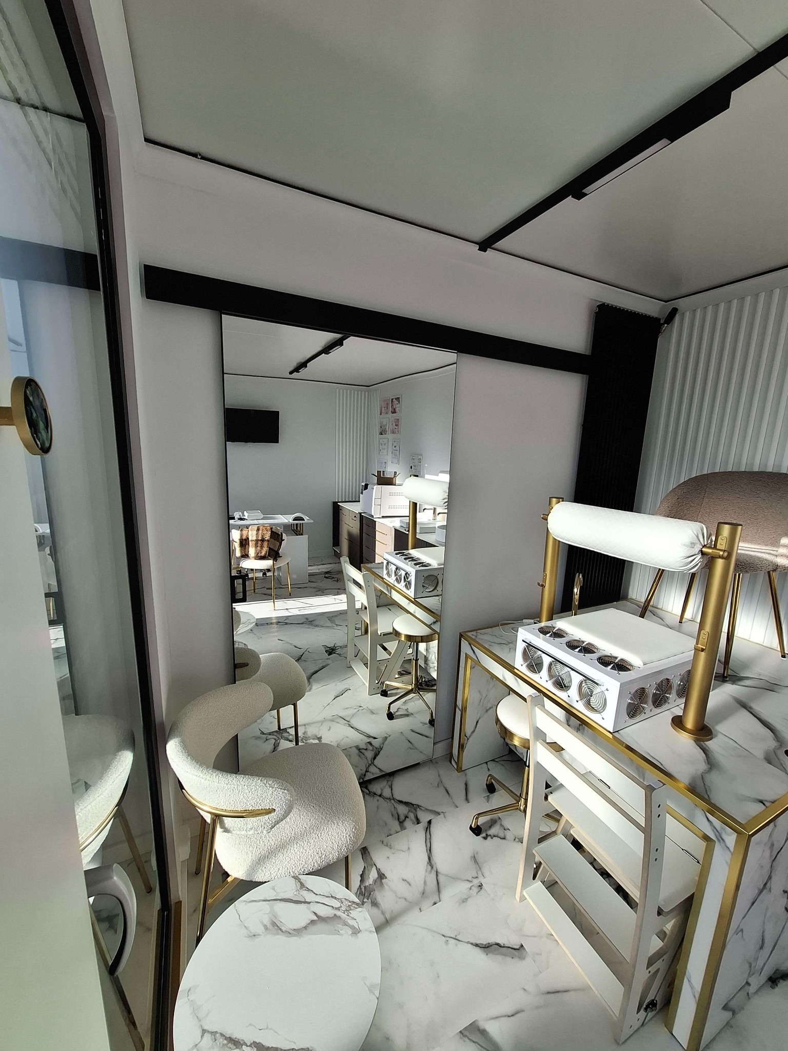 Nowoczesne wnętrze salonu kosmetycznego z marmurową podłogą i stolikami do manicure z białymi krzesłami na złotych nogach, widok przez lustro.