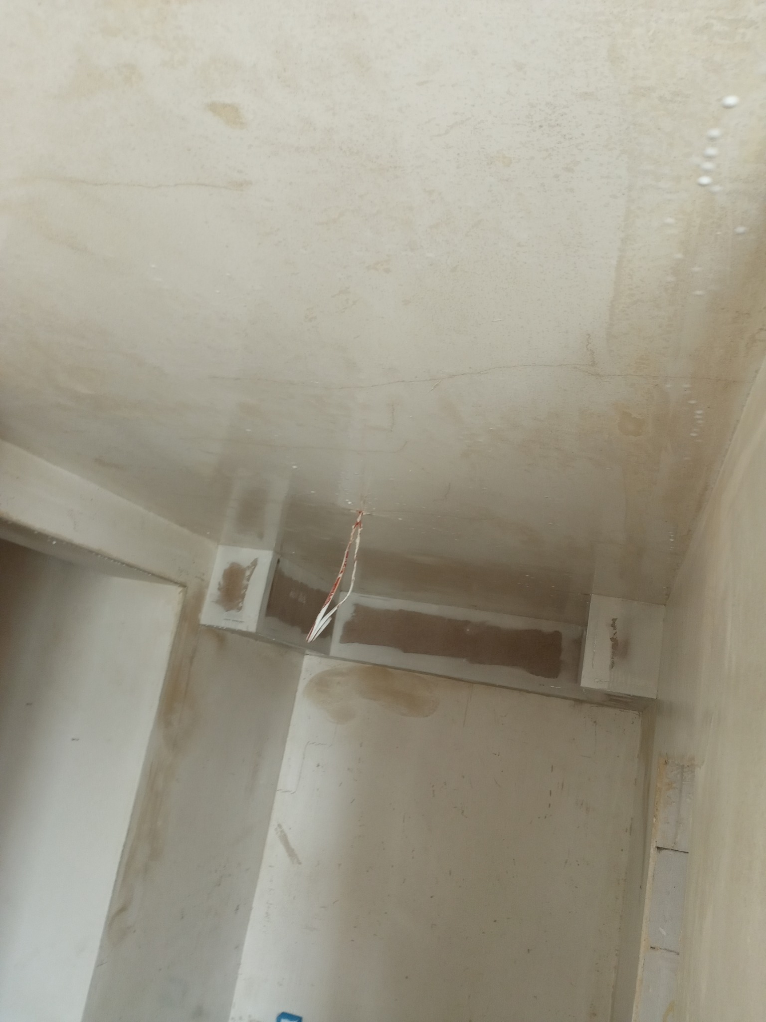 Wnętrze w trakcie prac wykończeniowych: świeżo nałożona gładź na suficie, wystające kable elektryczne, przygotowane ściany do dalszych prac. Widoczny fragment sufitu i ścian.