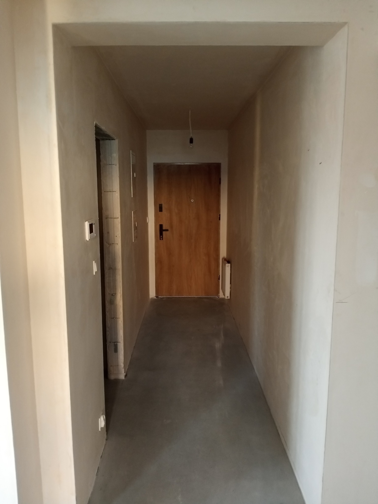 Korytarz w trakcie remontu: ściany po szpachlowaniu, widoczne wykończone futryny drzwi i surowa podłoga. Ujęcie na wprost, wnętrze do wykończenia.