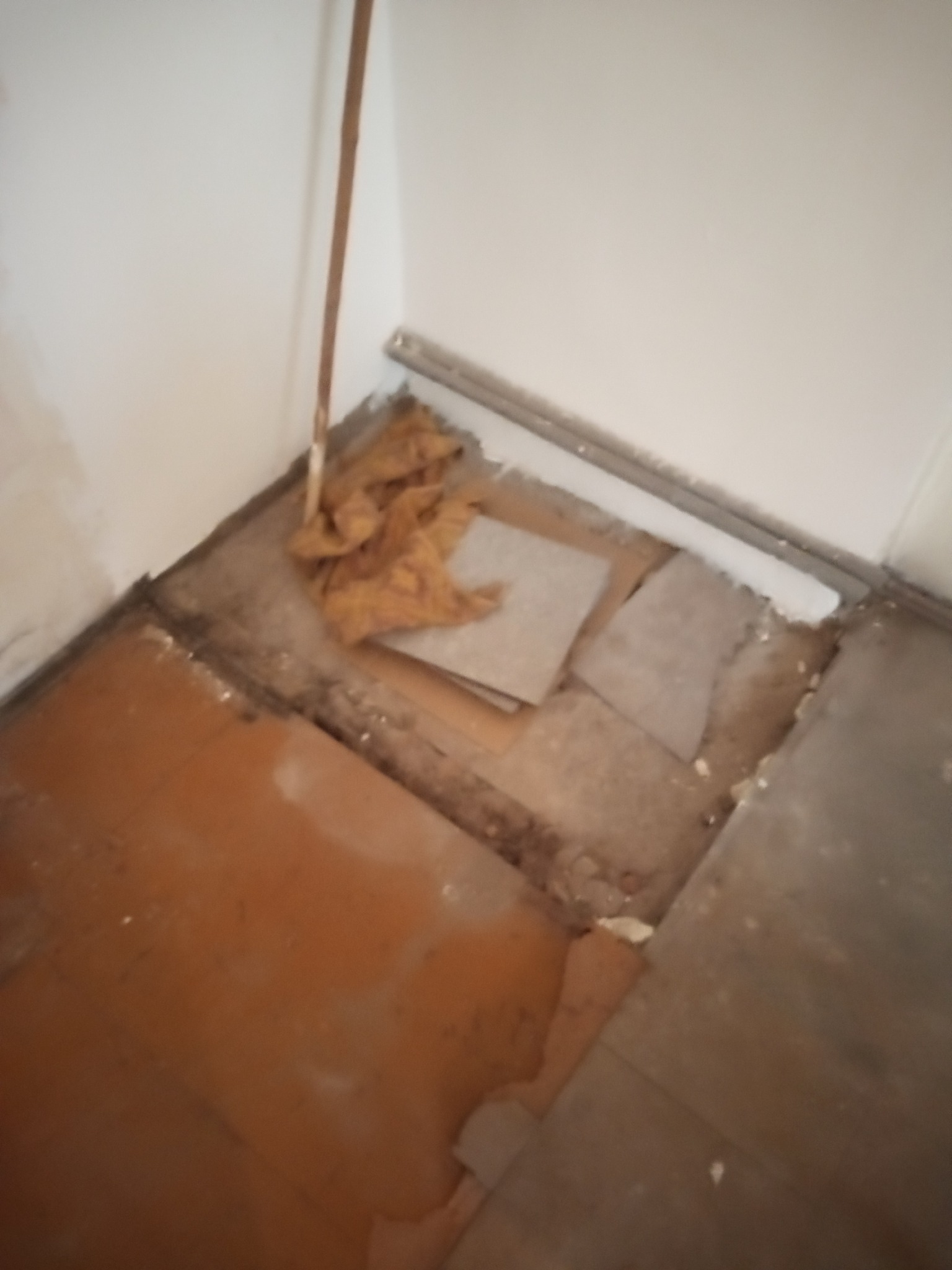 Fragment podłogi w trakcie demontażu. Widoczne stare panele, odsłonięta podłoga i listwa przypodłogowa. Przy ścianie leżą resztki materiału.