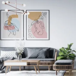 Wnętrze salonu z szarą sofą, drewnianym stolikiem kawowym i trzema oprawionymi plakatami na ścianie, w tym dwoma z abstrakcyjnymi rysunkami liniowymi i jednym z kolażem surrealistycznym.