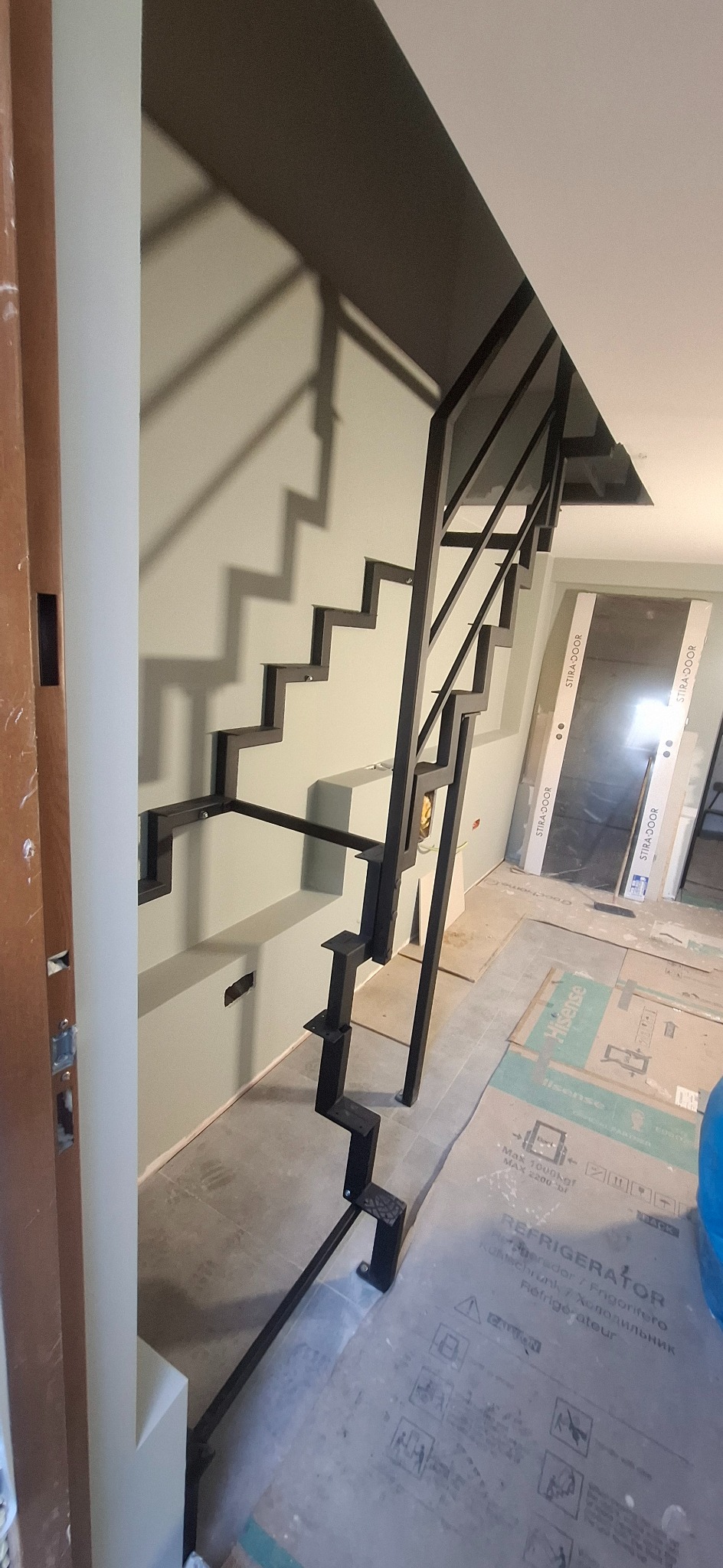 Nowoczesne, czarne schody z metalowymi stopniami i balustradą o geometrycznym designie, widoczne na tle jasnej ściany i podłogi w trakcie remontu.