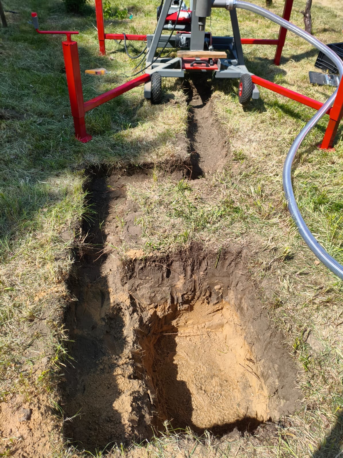 Wykop pod studnię głębinową z widoczną maszyną wiertniczą na trawiastym terenie, z przewodem doprowadzającym wodę. Etap wiercenia.