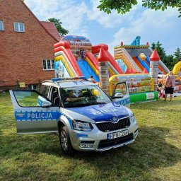 P&R Dmuchańce - Radiowóz policyjny z otwartymi drzwiami na trawie, w tle dmuchane zamki i zjeżdżalnie w słoneczny dzień.