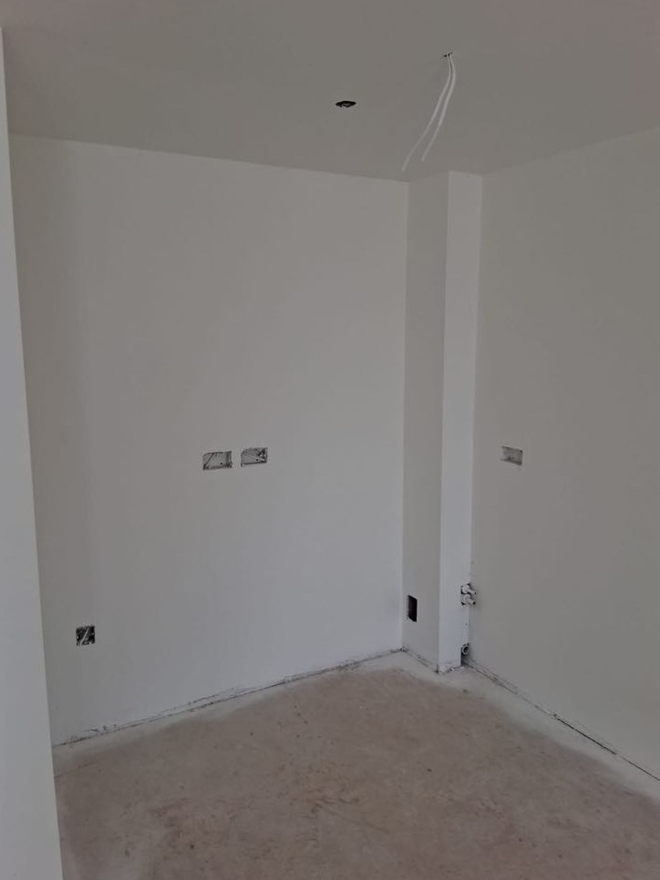Wnętrze pokoju po malowaniu na biało, widoczne puszki elektryczne i wystające przewody z sufitu, przygotowane do dalszych prac wykończeniowych.