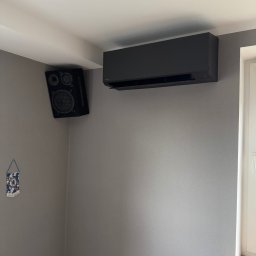 KLEKOCKI - Czarny klimatyzator ścienny Toshiba, zamontowany w rogu pokoju z szarą ścianą, obok głośnika i małej flagi Chelsea.