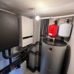 KLEKOCKI - Kotłownia z zamontowaną pompą ciepła Panasonic Aquarea, zbiornikiem buforowym Termica i naczyniami przeponowymi w kolorach czerwonym i białym.