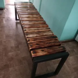 Metalowa ławka z drewnianymi szczeblami, opalana i lakierowana, na tle turkusowej ściany i korytarza.