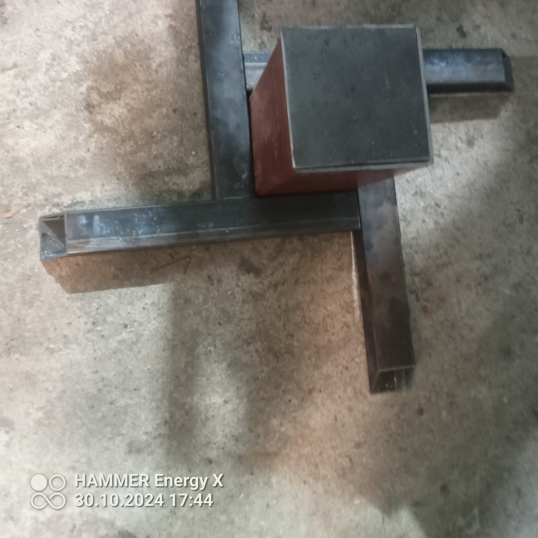 Konstrukcja spawana z profili stalowych o przekroju kwadratowym, z elementem podpory w kolorze rdzawym, na betonowej posadzce.